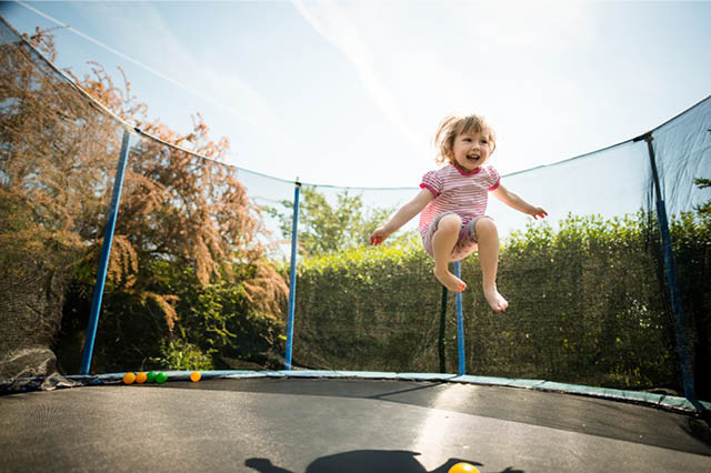 A little girl in a red-striped shirt and polka-dot shorts jumps up on a trampoline.
