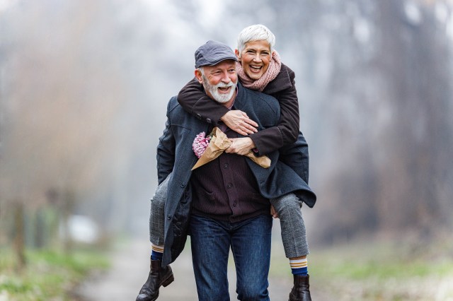 Happy senior couple having fun while piggybacking in winter day at the park. Copy space.