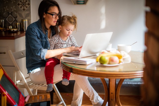 Photo of a little girl trying to help mom who is working on a computer at their dining table